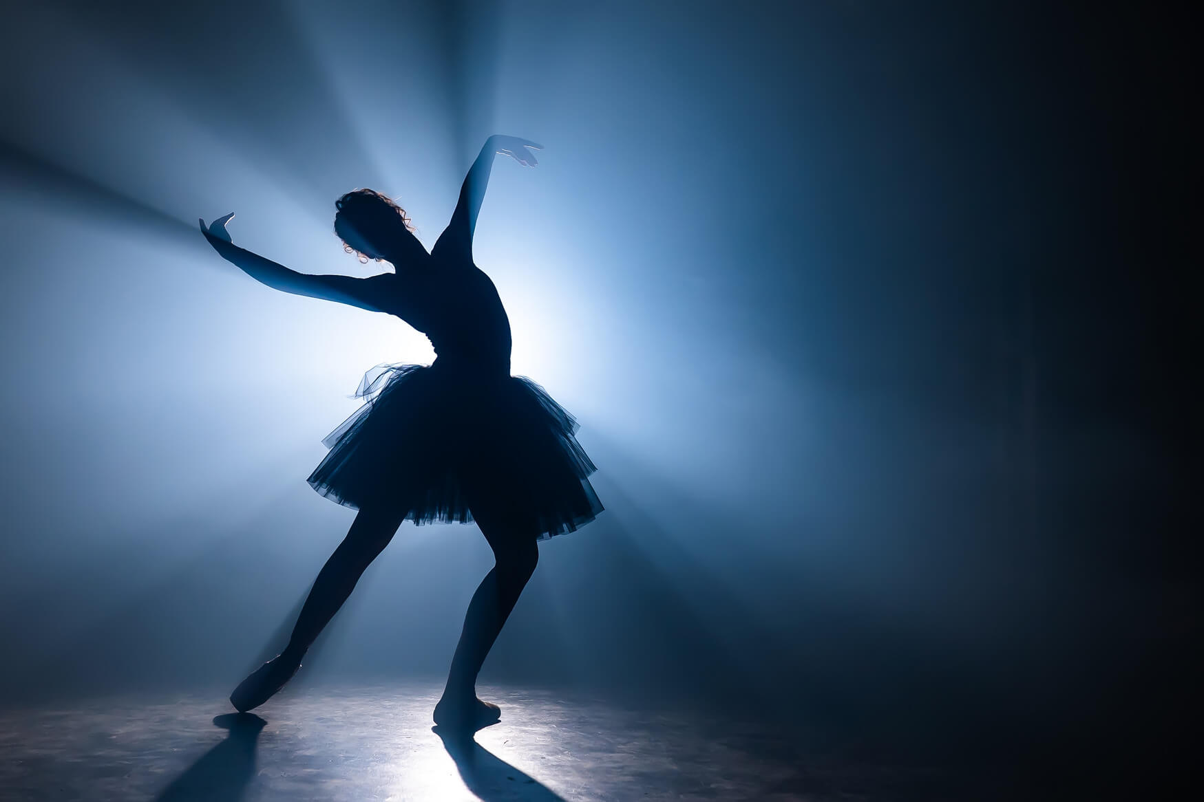 The Epic Dance Experience A ballerina in a tutu poses gracefully on stage, silhouetted against a bright blue light with rays shining outward, capturing the elegance of The Epic Dance Experience at Canada #1 Dance Competition. Canadian Dance Competition