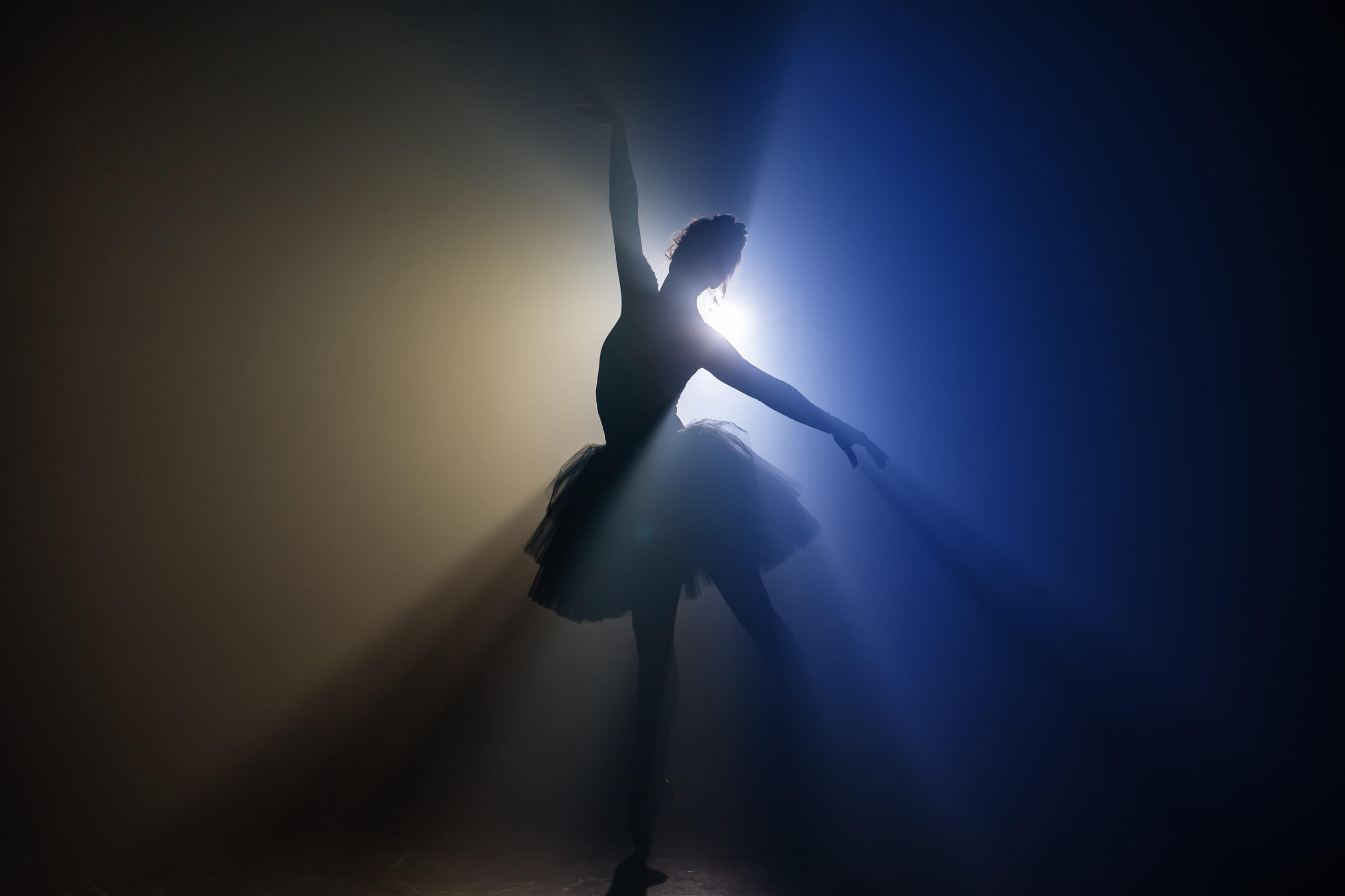The Epic Dance Experience Silhouette of a ballerina posing en pointe, one arm raised, against blue and yellow spotlights creating dramatic rays—capturing the elegance and excitement of The Epic Dance Experience at Canada’s #1 Dance Competition. Canadian Dance Competition