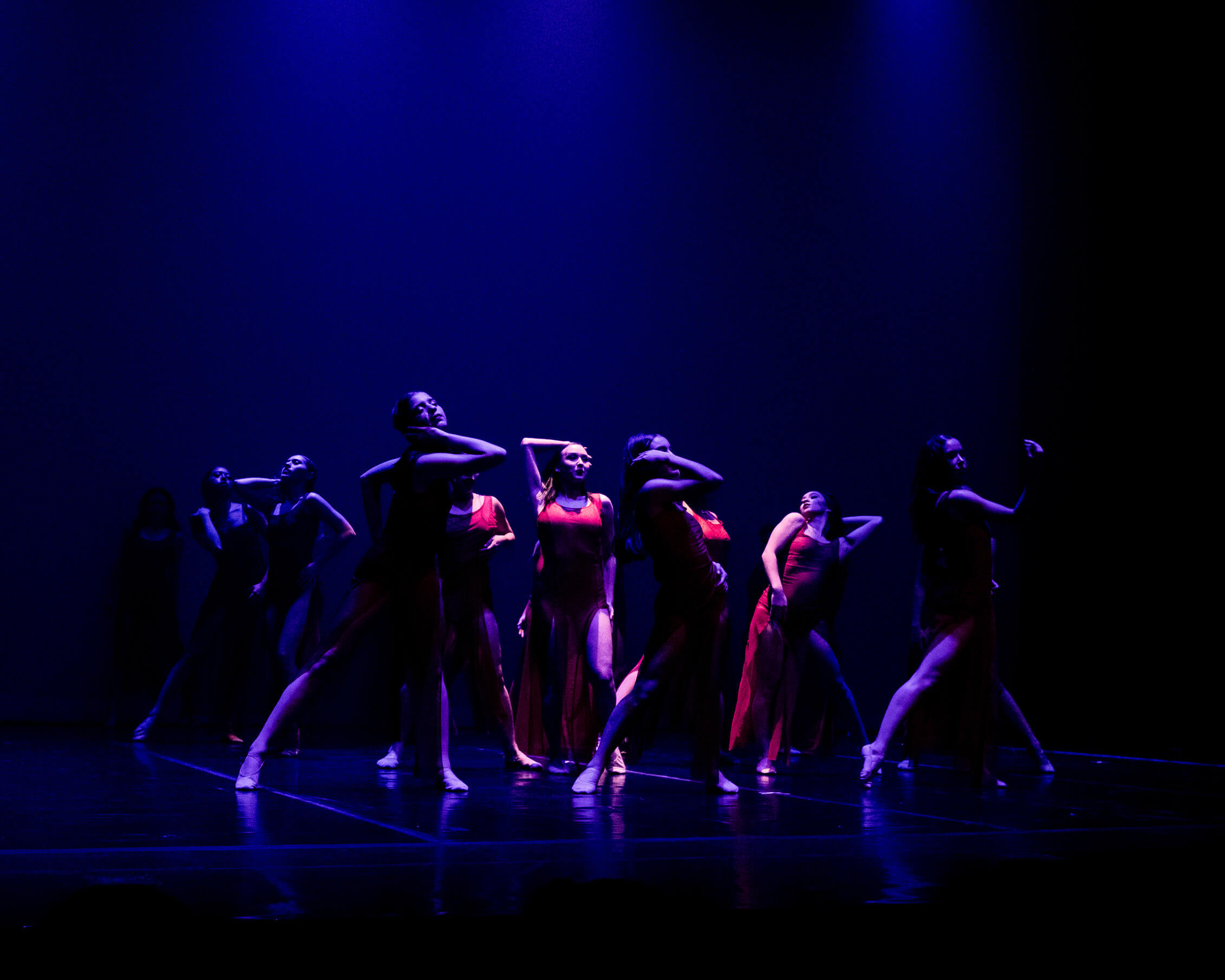 The Epic Dance Experience A group of dancers in red costumes perform on stage under blue lighting, posing with extended arms and legs at The Epic Dance Experience, Canada #1 Dance Competition. Canadian Dance Competition